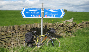 Directional signage for the Trans Pennine Trail next to a brick wall and a bicycle