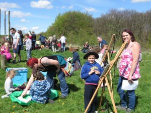 Children and adults painting on easels on a field
